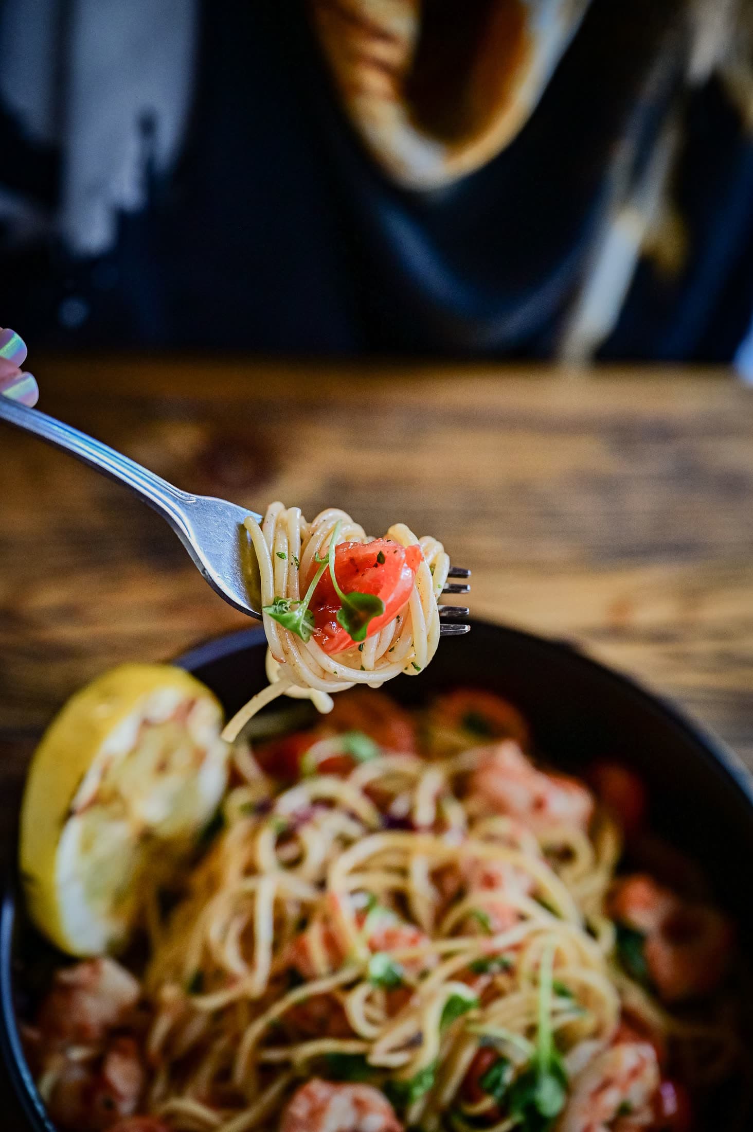 A fork lifting prawn spaghetti with cherry tomatoes