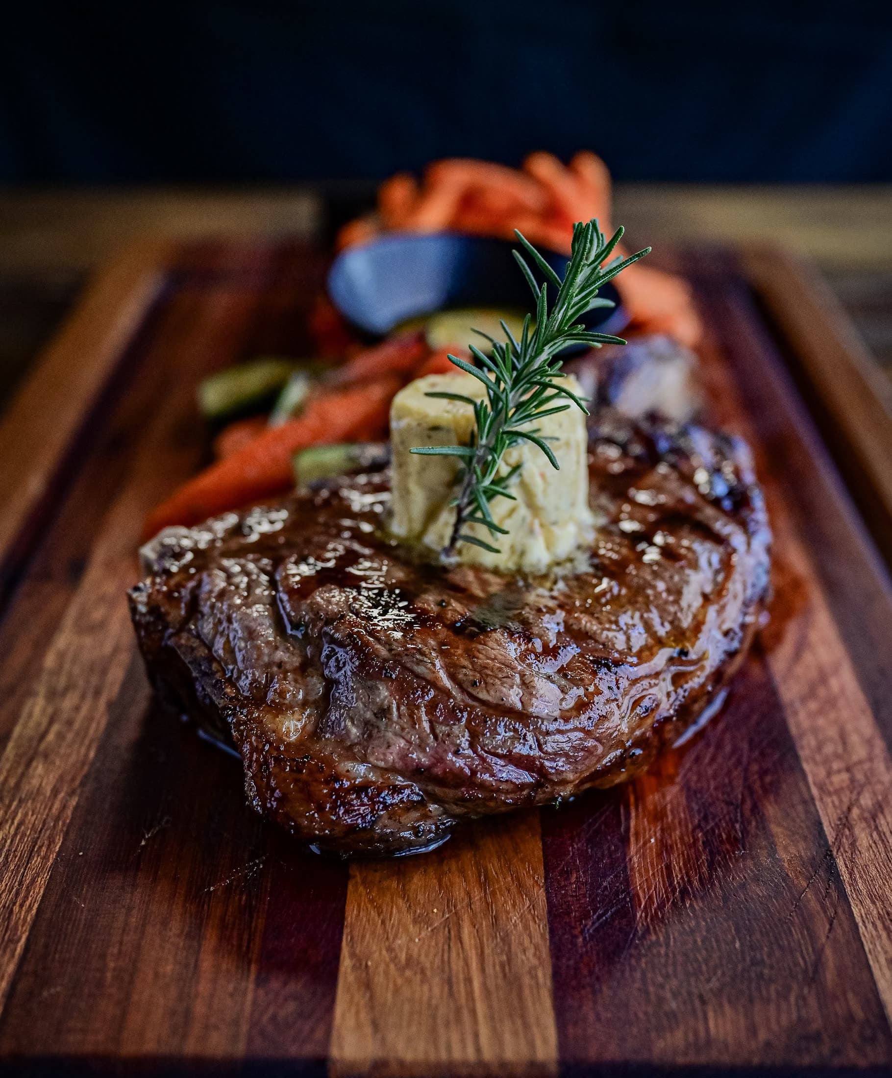 A grilled steak finished with herb butter on a wooden board